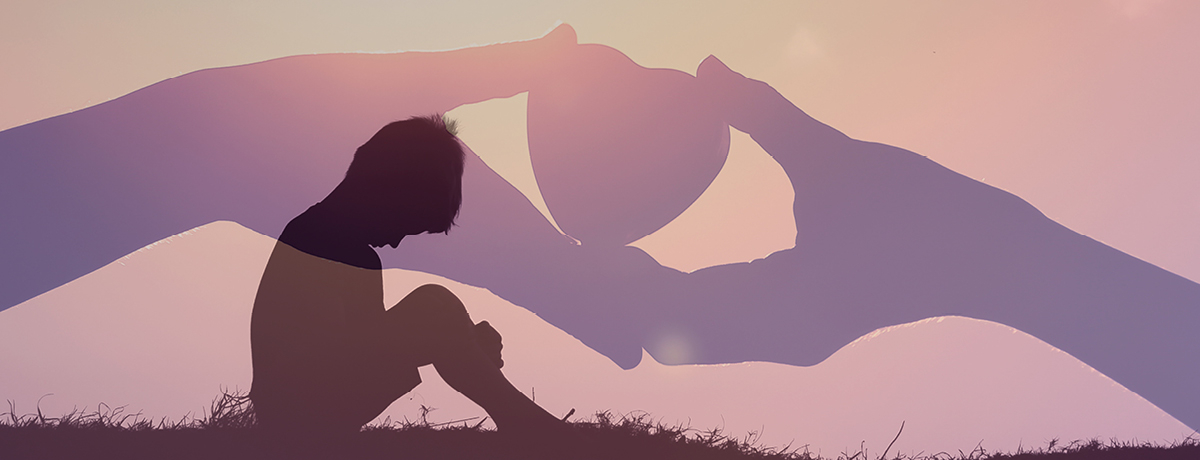 Dark silhouette sits with hands holding heart in backdrop