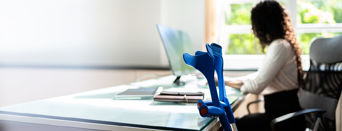 A woman sits at her computer with crutches placed next to her, representing disability.