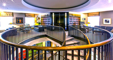 Top of a Staircase Featuring Two Large Black Doors with Bookshelves and Chairs on Each Side
