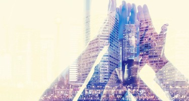 Group of hands put together in the air overlayed with a building in the background