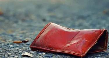 A close-up photograph of a weathered, empty red leather wallet lying abandoned.