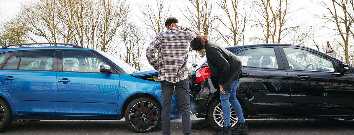 Two individuals examining damage at a car accident scene
