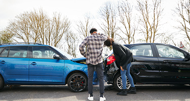 Two individuals examining damage at a car accident scene