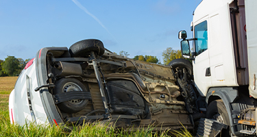 Car turned on its side in grass after collision with truck