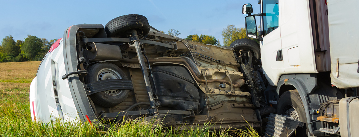 Car turned on its side in grass after collision with truck