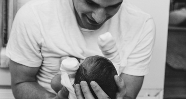 Man holds his newborn with a black and white filter over the photo