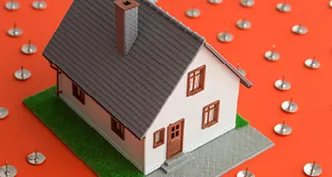 Miniature house model on orange background surrounded by thumbtacks representing foreclosure