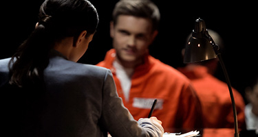 A Lady in a Suit Taking Notes Across from a Man in an Orange Jumpsuit at a Table