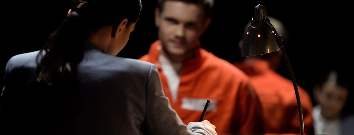 A Lady in a Suit Taking Notes Across from a Man in an Orange Jumpsuit at a Table